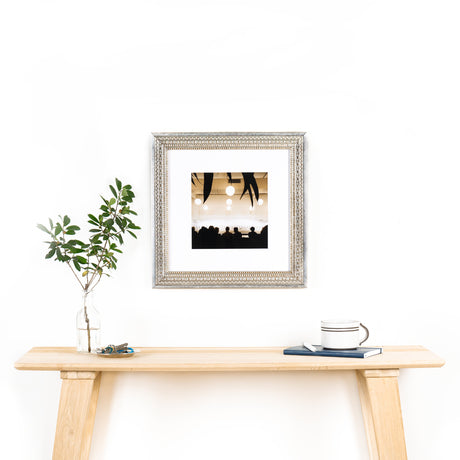 photograph in a brighton wide pattern silver frame on a white wall above table with plants in a glass vase and key tray with a coffee cup on top of a notebook