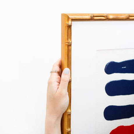 Hand holding navy and red abstract art in gold bamboo frame angle