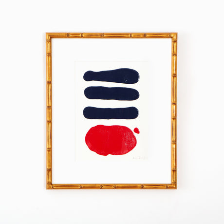 Navy and red abstract art in gold bamboo frame on white wall