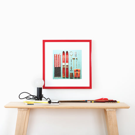 Ski and flag art in red frame above table with arrows and lamp